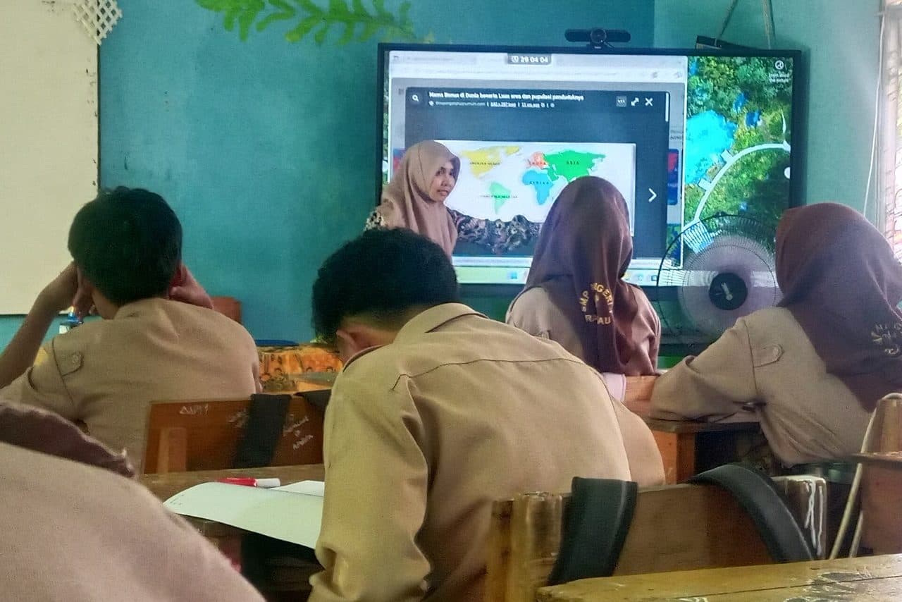 Guru mengajar di depan papan interaktif sementara siswa SMP berseragam mengikuti pelajaran dari bangku mereka