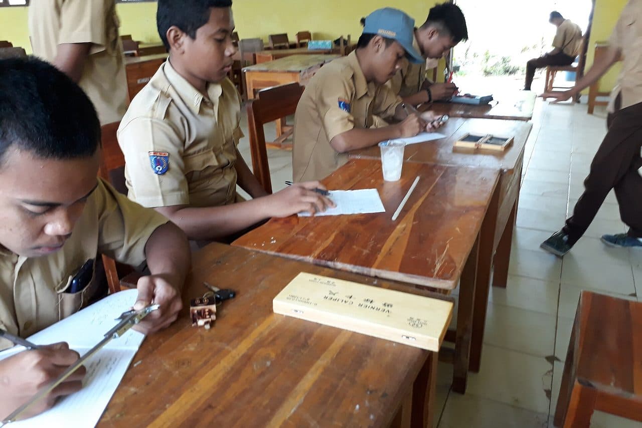 Beberapa siswa SMK berseragam mengisi formulir di atas meja kayu saat ujian praktik di sekolah